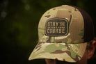 Camouflage cap with 'Stay the Course' patch on a blurred natural background