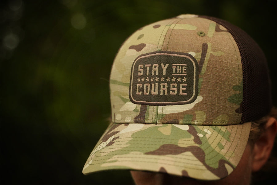 Camouflage cap with 'Stay the Course' patch on a blurred natural background