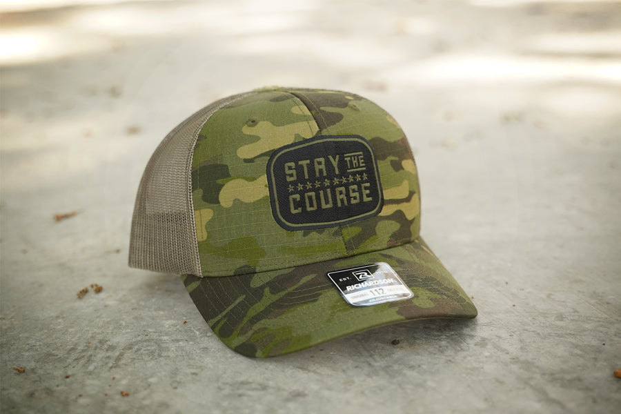 Camouflage cap with 'Stay the Course' patch on a concrete surface