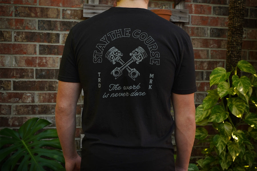 Person wearing a black t-shirt with a motivational quote on the back, standing against a brick wall.