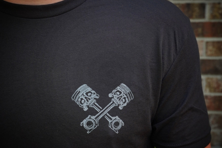 Person wearing a black t-shirt with a gray engine piston design on a brick wall background