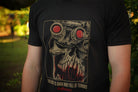Person wearing a black t-shirt with tan and red graphic print and the words "the night is dark and full of terrors", in an outdoor setting.