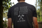 Person wearing a black t-shirt with 'No Risk No Story' text and graphic, outdoors.