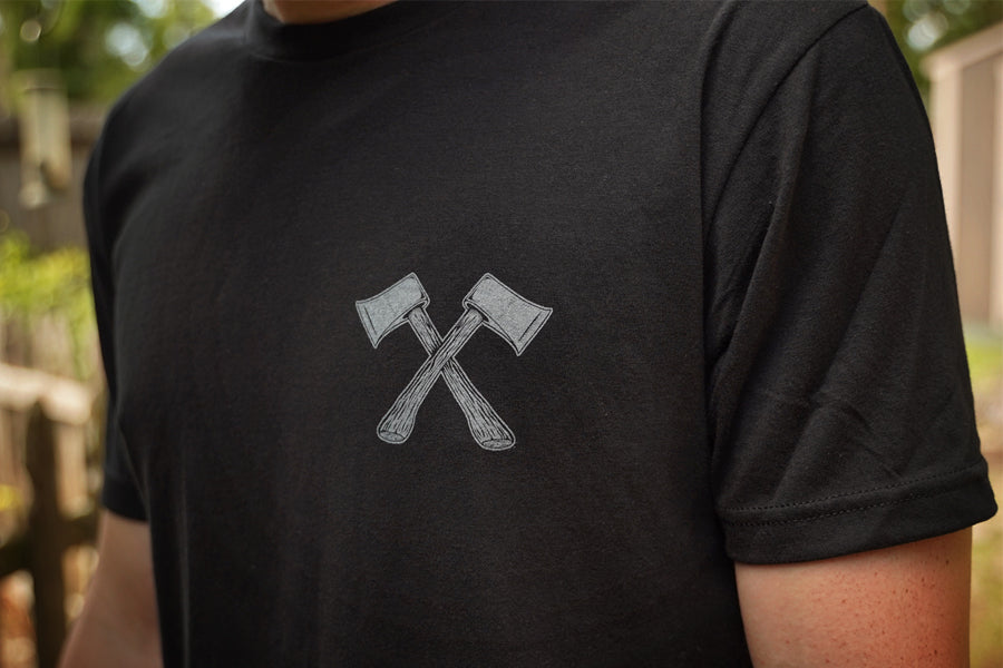Person wearing a black t-shirt with a graphic of two crossed axes on a blurred outdoor background