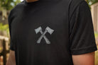 Person wearing a black t-shirt with a graphic of two crossed axes on a blurred outdoor background