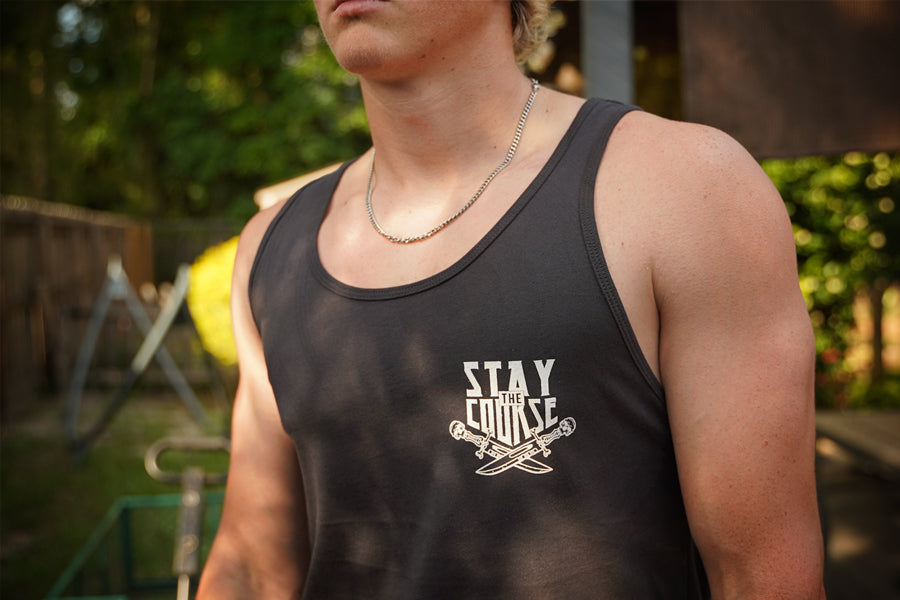 A person wearing a dark gray tank top with white text and dagger graphics on the front left chest.