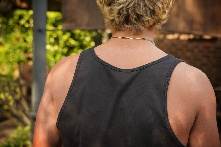 Person wearing a gray tank top with a blurred outdoor background