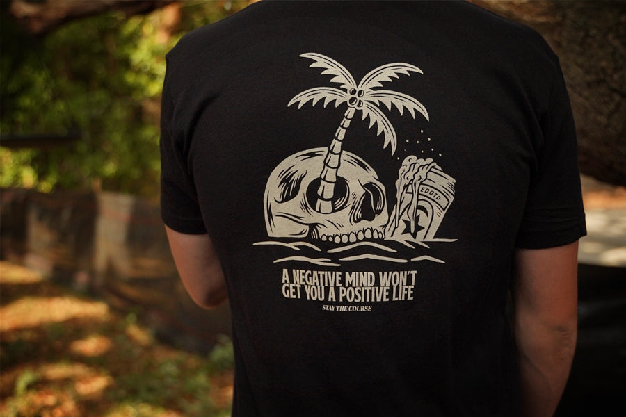 Person wearing a black t-shirt with a skull and palm tree design and text.