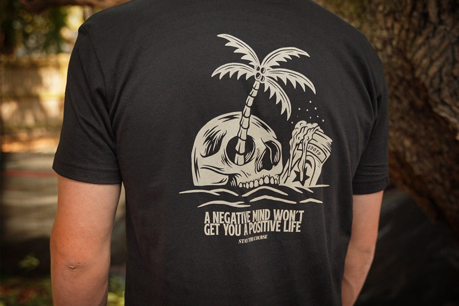 Black t-shirt with a skull and palm tree design on the back, featuring text.