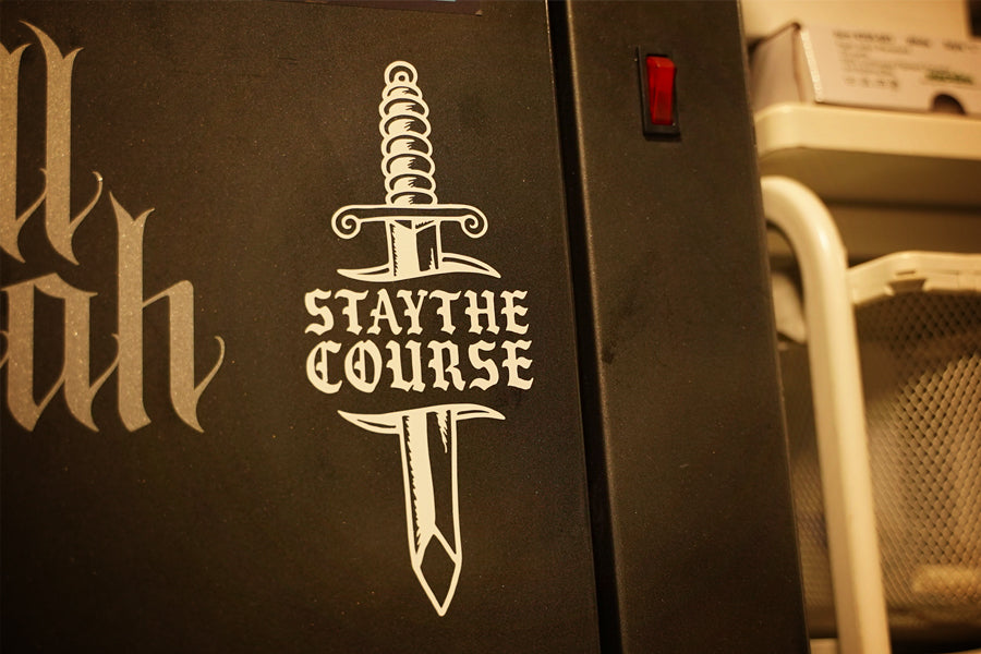 White vinyl decal of dagger and "stay the course" on metal cabinet