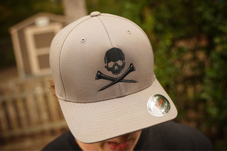 Gray cap with skull and golf tees design worn by a person, blurred background