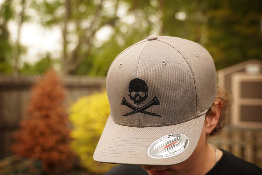Gray cap with skull and golf tees design worn by a person outdoors.
