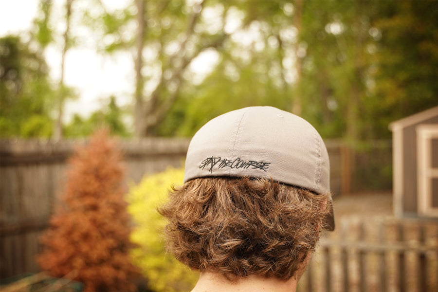 Person wearing a cap with Stay the Course, standing in a backyard with trees and a fence.