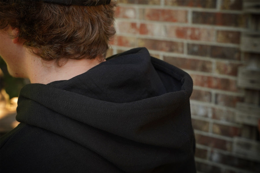 Person wearing a black hoodie with a brick wall in the background
