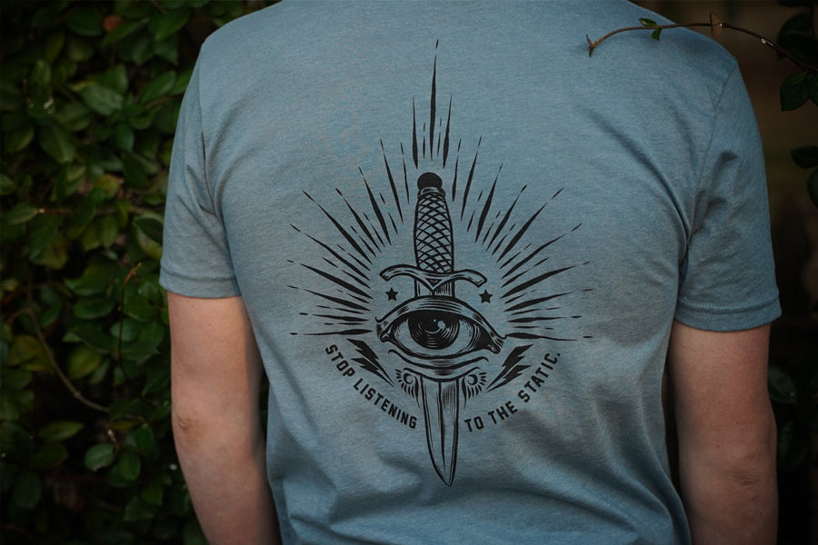 Person wearing a blue t-shirt with a black graphic design on the back, against a blurred green background.