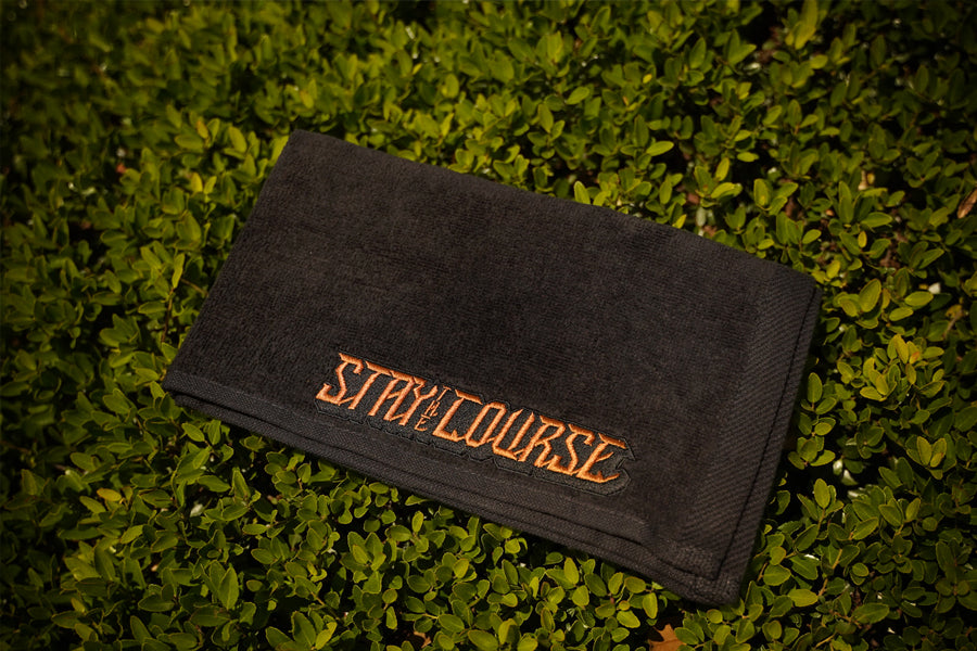 Black towel with 'Stay on the Course' text on grass