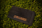 Black towel with 'Stay on the Course' text on grass