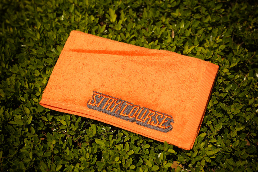Orange towel with 'STAY the COURSE' branding on grass