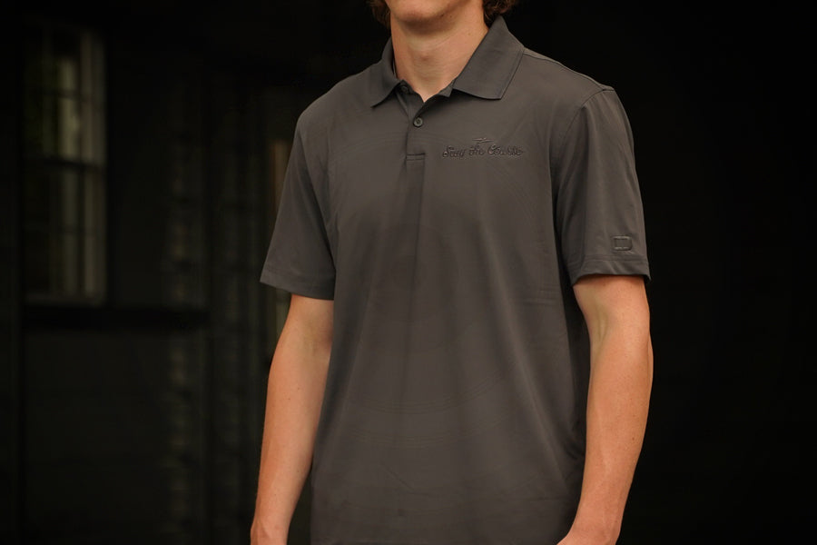 Person wearing a dark gray polo shirt with brand logos on a black background