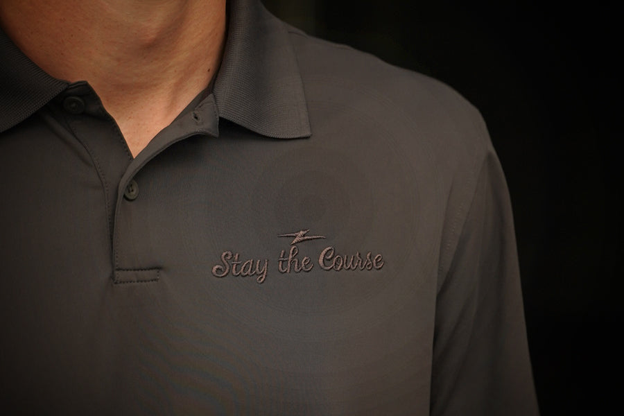 Dark gray polo shirt with 'Stay the Course' embroidery on a black background
