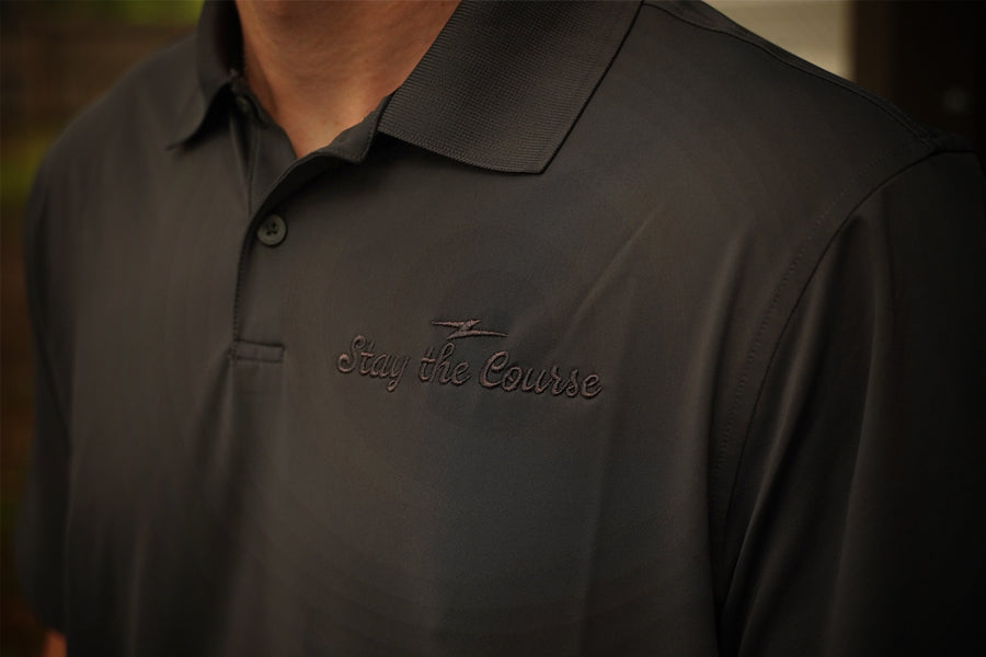 Dark polo shirt with 'Stay the Course' text on a blurred background