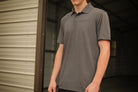 Person wearing a gray polo shirt with a brand logo, standing in front of a metal building