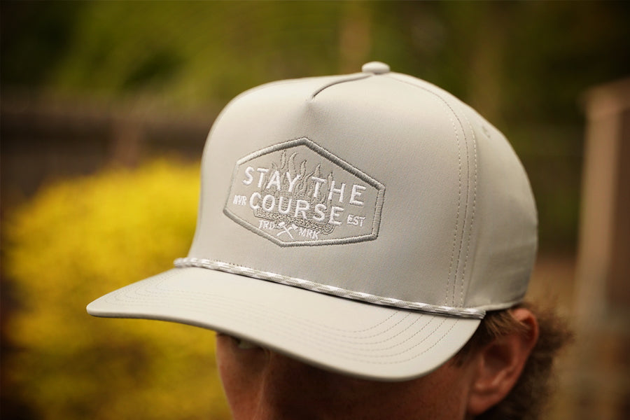 Gray cap with 'Stay the Course' logo worn by a person outdoors