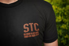 Black t-shirt with 'STC' logo worn by a person, against a blurred green background