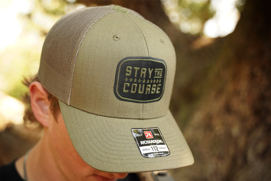 Olive green cap with 'Stay the Course' text and Richardson logo on a blurred natural background