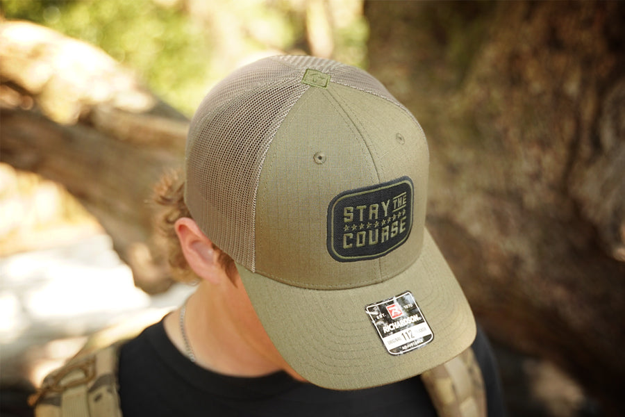 Person wearing a cap with 'Stay the Course' logo in a natural setting
