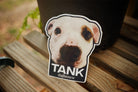 Sticker of a dog's face with 'TANK' and 'staythecourse' text on a wooden surface.