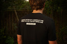 Person wearing a black t-shirt with white print that says "Being hated by losers is the price you pay for not being one, Stay the Course", in an outdoor setting