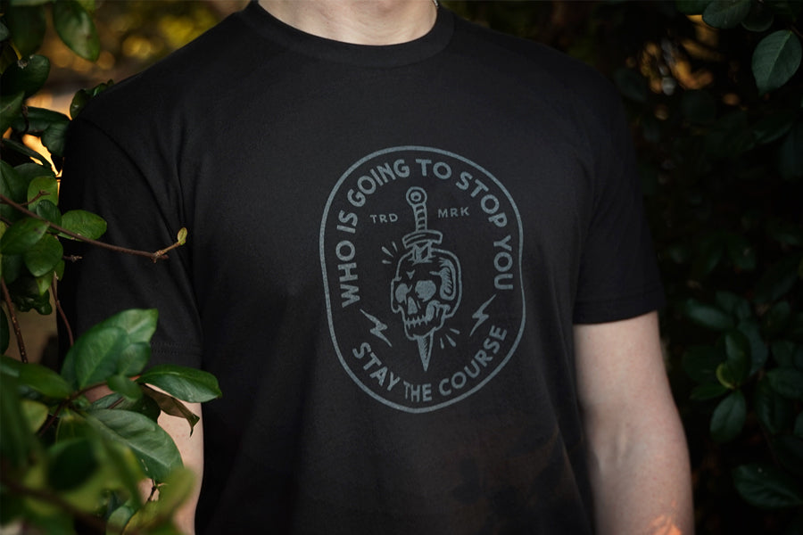 Person wearing a black t-shirt with a skull and sword graphic and text.