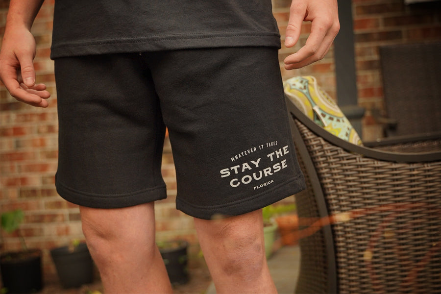 Person wearing black shorts with 'Stay the Course' text, standing outdoors.