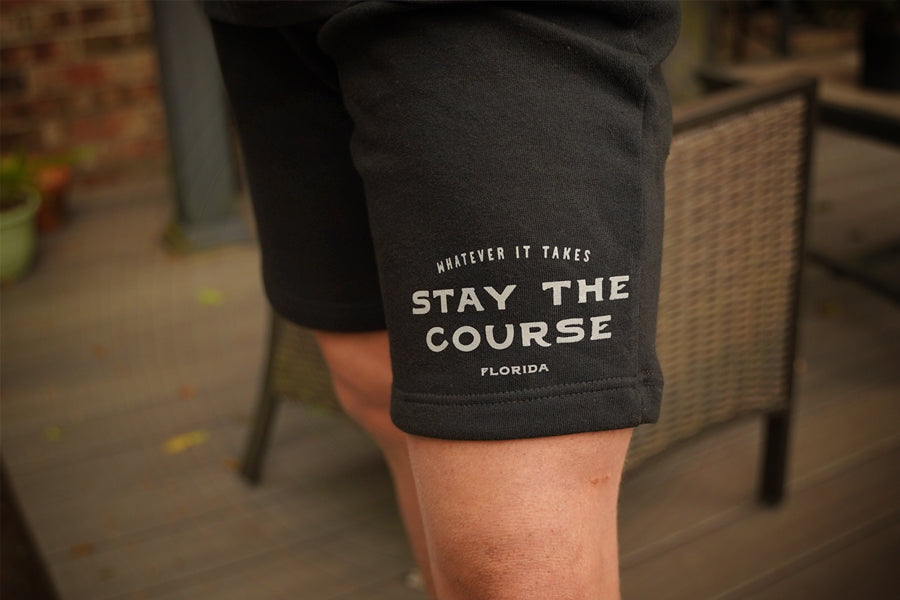 Black shorts with 'Stay the Course Florida' text on a blurred outdoor background