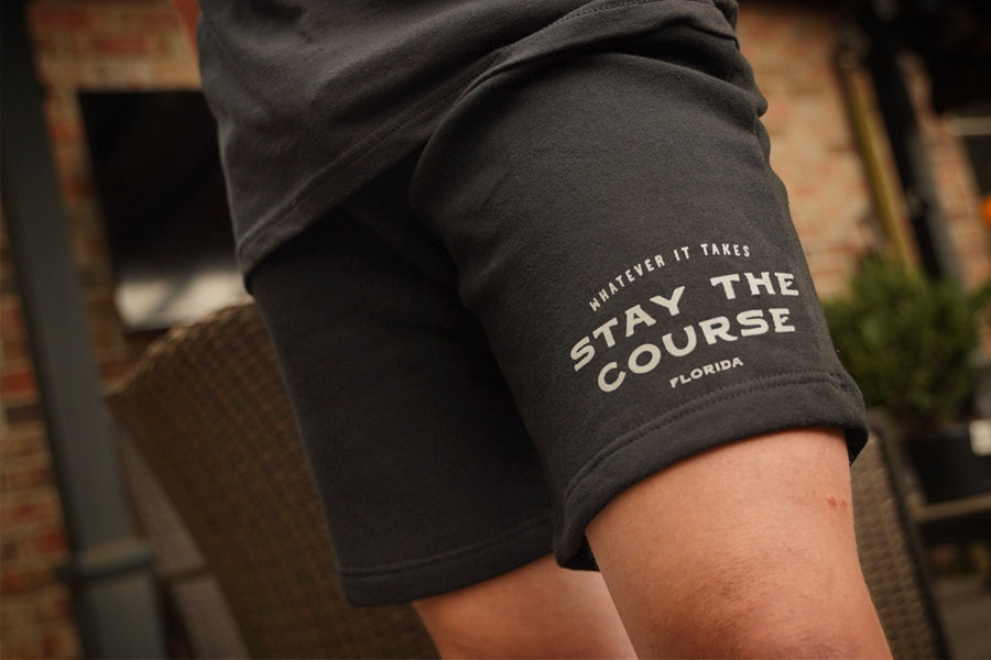 Person wearing black shorts with 'Whatever it takes - Stay the Course' text, blurred background