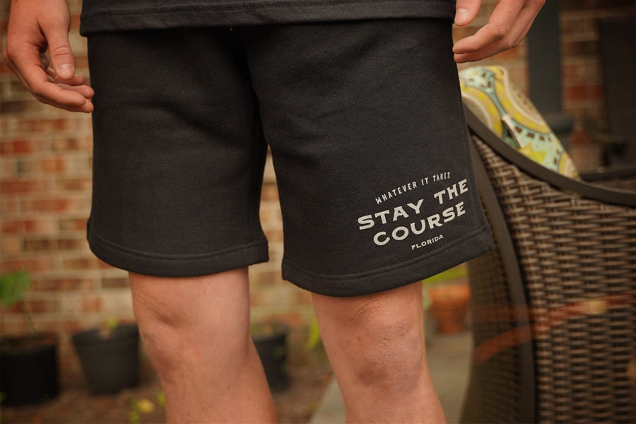 Black shorts with 'Stay the Course' text worn by a person, outdoor setting.
