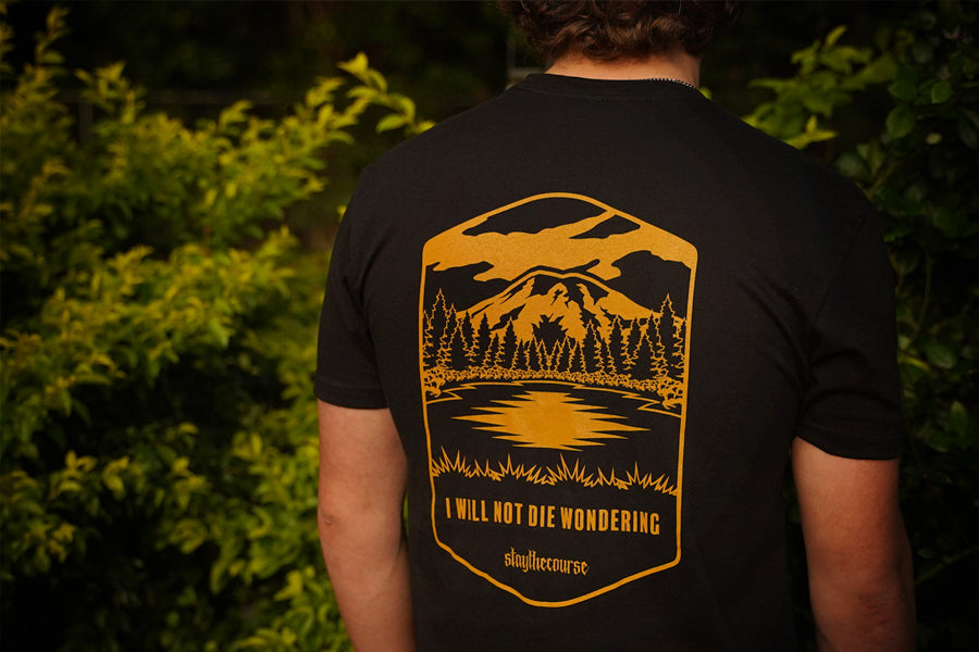 Person wearing a black t-shirt with a golden yellow nature-themed design and text.